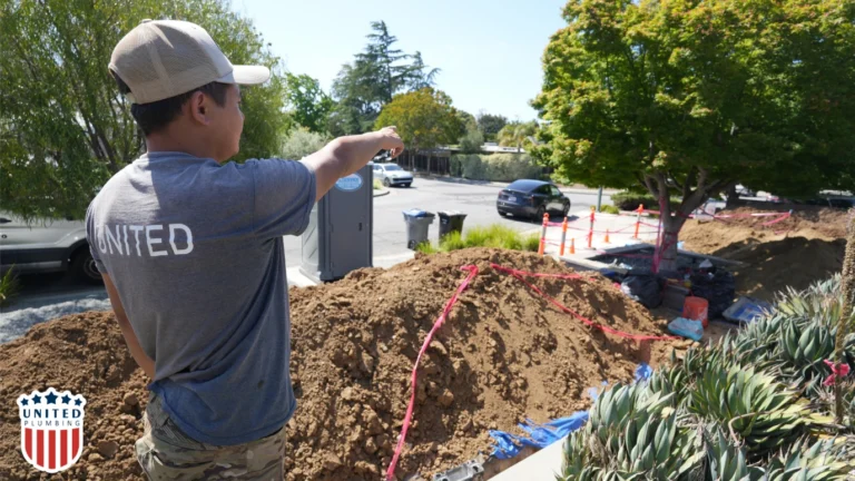 Technician from United Plumbing pointing at an active sewer line excavation site near a residential street.