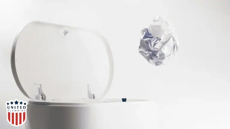 Crumpled paper going into a bathroom trash can, showing how to prevent toilet clogs by throwing trash away instead of flushing.