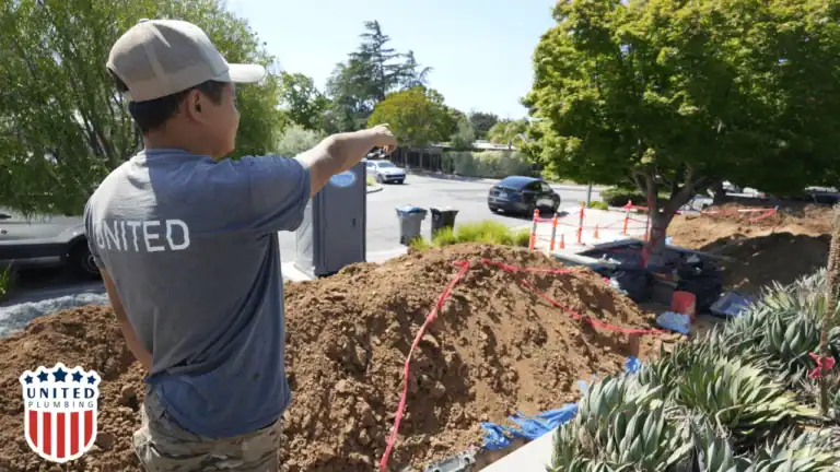 Professional plumber at a residential work site, pointing toward sewer line excavation for clogged drain repair.