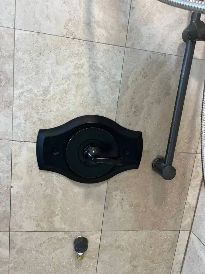 Black shower control handle and trim plate installed on a tiled bathroom wall